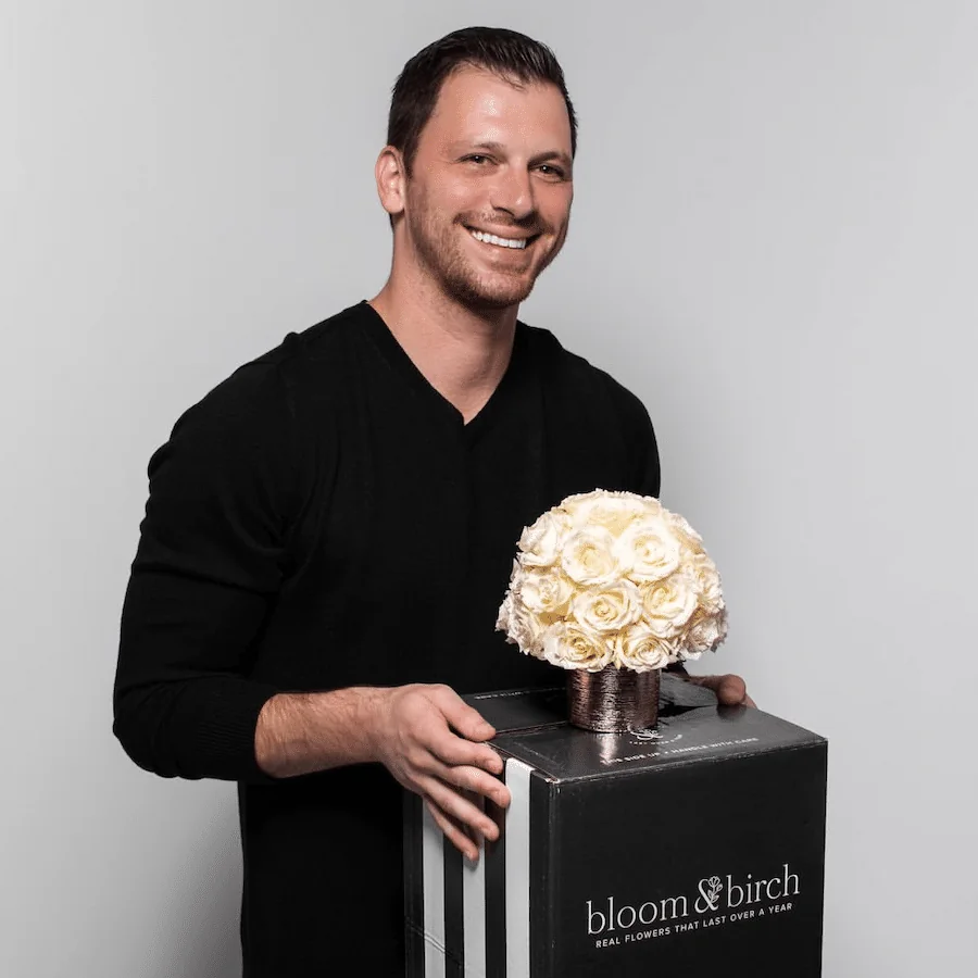 A man holding a floral arrangement in a black Bloom and Birch presentation box