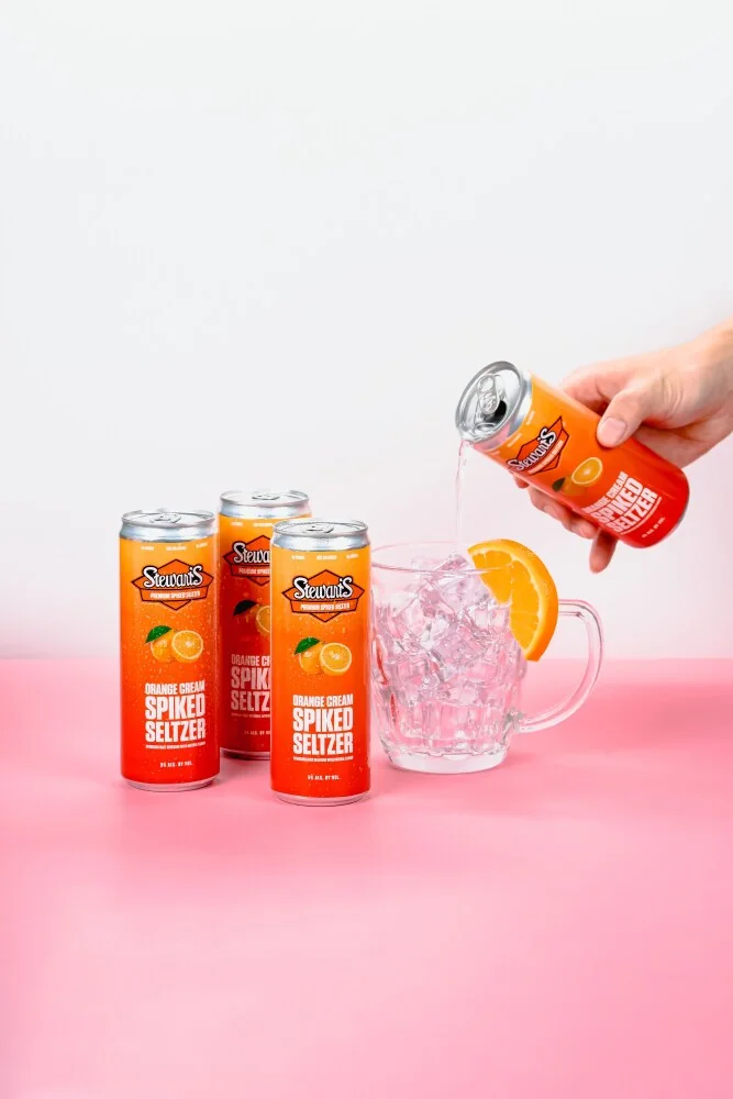 Orange Cream cans beside a hand pouring seltzer into a glass